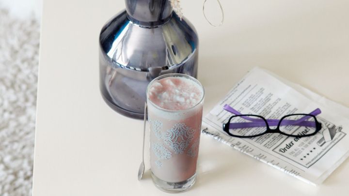 Ein Glas mit kaltem Kaffeegetr&auml;nk und Joghurt steht auf einem Tisch neben einer Vase und einer Zeitung.