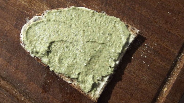 Ein St&uuml;ck Brot, bestrichen mit gr&uuml;ner B&auml;rlauchbutter, liegt auf einem Holztisch und wirkt appetitlich und frisch.