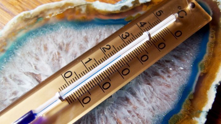 Ein Thermometer liegt auf einem bunten Mineralstein und zeigt hohe Temperaturen, was Schlafen trotz Sommerhitze erschwert.