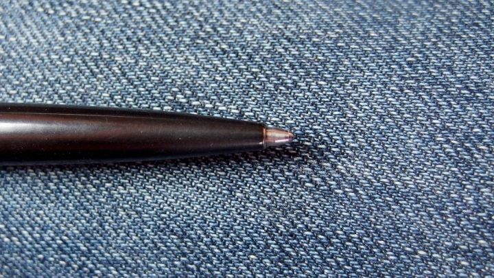 Ein Kugelschreiber liegt auf einem blauen Jeansstoff, wobei die Spitze des Stifts auf einem kleinen Riss zeigt.
