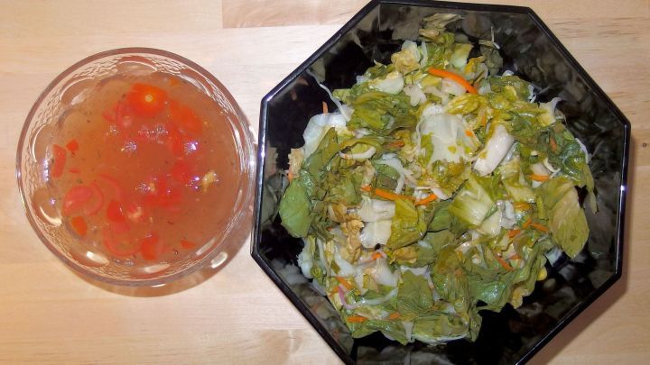 Frischer Salat in einer schwarzen Sch&uuml;ssel neben einer transparenten Sch&uuml;ssel mit Salatso&szlig;engew&uuml;rz.