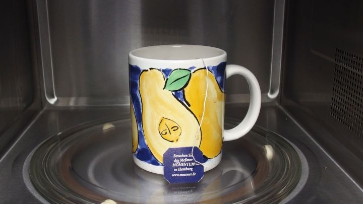 Eine bunte Tasse steht auf dem Drehteller der Mikrowelle und wird f&uuml;r das Erw&auml;rmen von Getr&auml;nken genutzt.