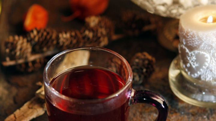 Ein Glas Gl&uuml;hwein steht auf einem rustikalen Tisch, umgeben von Kerzenlicht und weihnachtlichen Dekorationen.