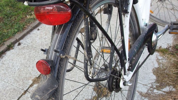 Ein Fahrrad steht auf einem Gehweg. Jemand nutzt Nagellackentferner, um Schmutz an den Reifen zu reinigen.