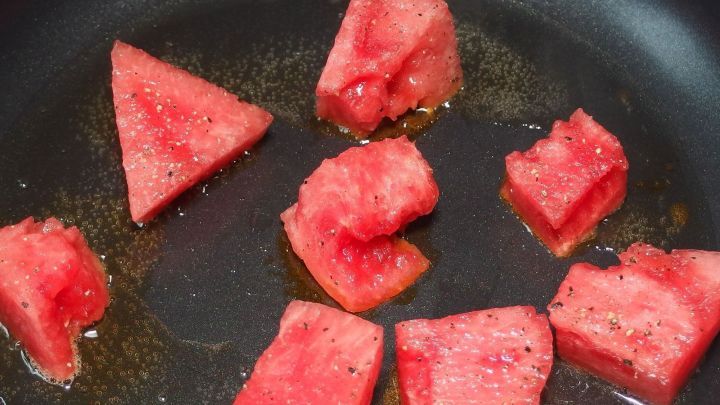 Saftige Melonenst&uuml;cke braten in einer Pfanne, um eine ungew&ouml;hnliche Beilage zu kreieren. Das &Ouml;l brutzelt um die St&uuml;cke.