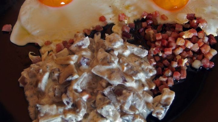 Ein cremiges Rahm-Champignon-Gericht wird zusammen mit knusprigem Speck und zwei sonnengelben Spiegeleiern serviert.