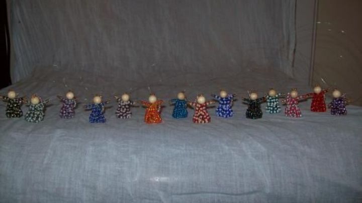 Bunte Engel aus Rocailles stehen in einer Reihe, umgeben von einem neutralen Hintergrund, der die Figuren betont.