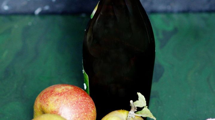 Eine Flasche Apfelessig steht neben frischen &Auml;pfeln auf einem gr&uuml;nen Hintergrund, ideal f&uuml;r die Pflege reiner Haut.