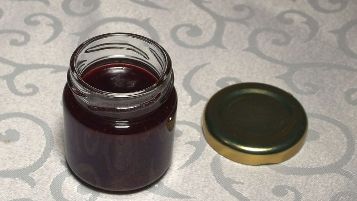 Ein Glas frische Marmelade steht auf einem gemusterten Tisch, der Deckel liegt daneben, bereit zum Einf&uuml;llen.