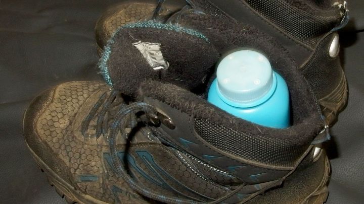 Wanderschuhe sind schmutzig und tragen ein Flaschchen Babypuder, um Blasen beim Wandern zu vermeiden, vor einem schwarzen Hintergrund.