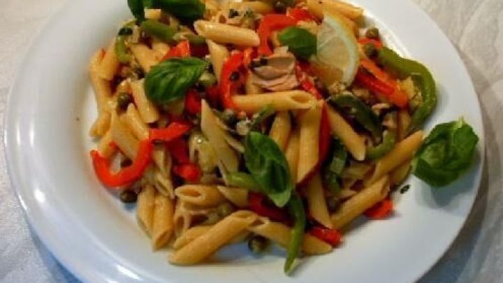 Penne sizilianisch liegt auf einem wei&szlig;en Teller, garniert mit frischem Basilikum, Paprika und einer Zitronenscheibe.