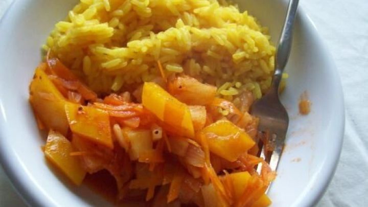 Gelber Reis ist sorgf&auml;ltig auf einem Teller angerichtet, erg&auml;nzt von einer s&uuml;&szlig;-sauren So&szlig;e aus buntem Gem&uuml;se, auf einem wei&szlig;en Tisch.