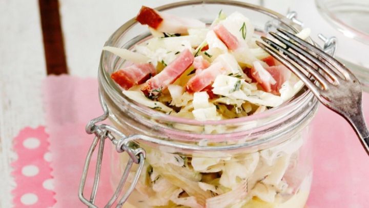 Ein Glas Murmeltiers Wei&szlig;kohl-Salat mit frischem Gem&uuml;se und einem Forke steht auf einem rosa Tischl&auml;ufer.