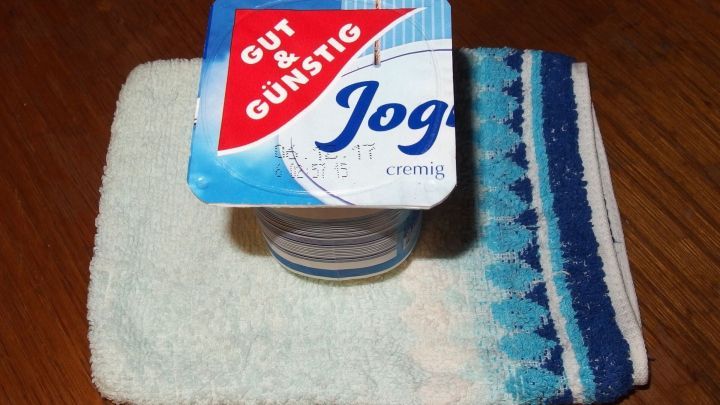 Ein Joghurtbecher steht auf einem kleinen Handtuch. Der Kontext ist eine einfache, saubere Oberfl&auml;che.