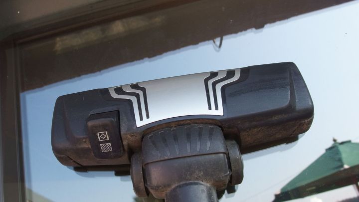 Ein Staubsauber reinigt Fensterfl&auml;che und entfernt Staub, w&auml;hrend er auf einem Fensterrahmen in einem sonnigen Au&szlig;enbereich steht.