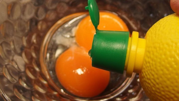 Zwei Eigelb liegen in einer Sch&uuml;ssel, w&auml;hrend frischer Zitronensaft dar&uuml;ber gepresst wird, um M&uuml;rbeteig aufzupeppen.