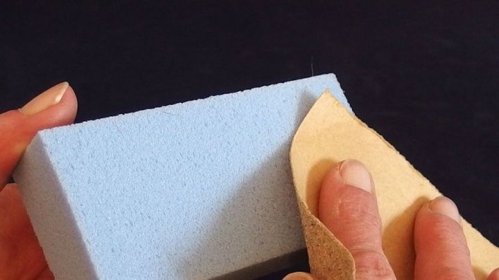 Ein blauer Bimsstein wird mit einem hellen Schwamm gereinigt, w&auml;hrend die H&auml;nde ihn in einem dunklen Umfeld halten.