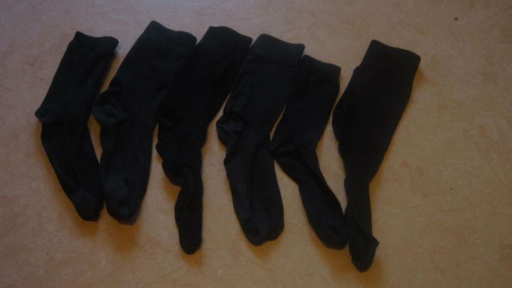 Sechs schwarze Socken liegen ordentlich nebeneinander auf einem hellen Boden, ideal f&uuml;r den Kauf von gleichen Sockenpaaren.