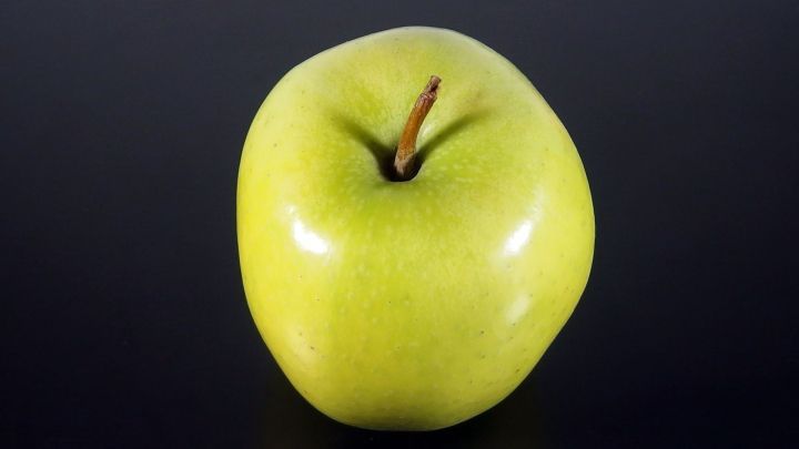 Ein gr&uuml;ner Apfel steht auf einem schwarzen Hintergrund, symbolisiert gesundes Essen zur Senkung des Cholesterinspiegels.