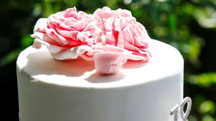 Eine festliche Torte mit kandierten Bl&uuml;ten oben, umgeben von gr&uuml;nen Pflanzen im Hintergrund.