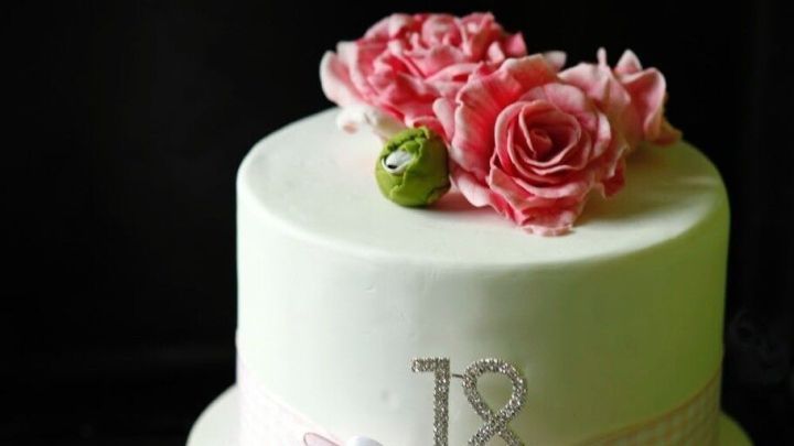 Eine elegante Zuckertorte mit einer dekorativen Schleife und Rosenbl&uuml;ten steht im Fokus, umgeben von dunklem Hintergrund.