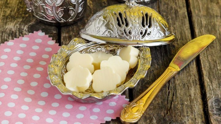 Pr&auml;chtige silberne Butterdosen stehen auf einer rustikalen Holzoberfl&auml;che, w&auml;hrend feine Butterst&uuml;ckchen bereitliegen.