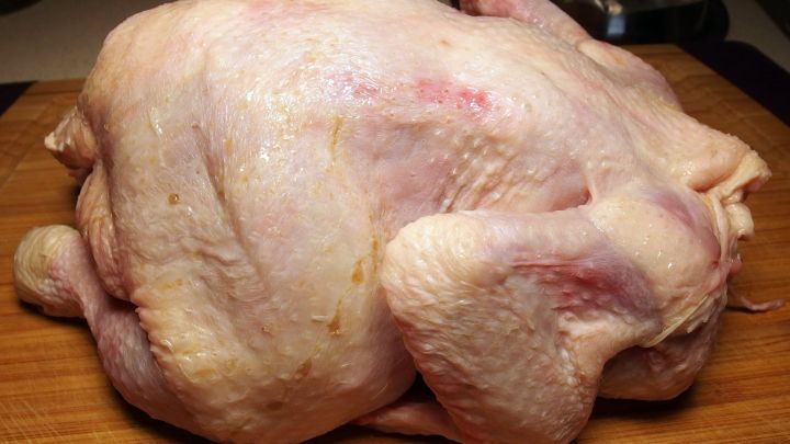 Ein H&uuml;hnchen liegt auf einem Holzbrett, bereit, mit frischem Zitronensaft einreibend zu werden.