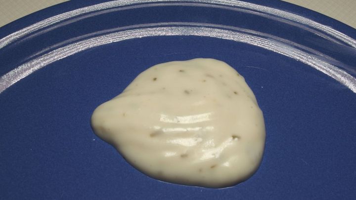 Eine cremige Knoblauchso&szlig;e liegt auf einem blauen Teller, bereit zum Servieren, in einer neutralen K&uuml;chensituation.