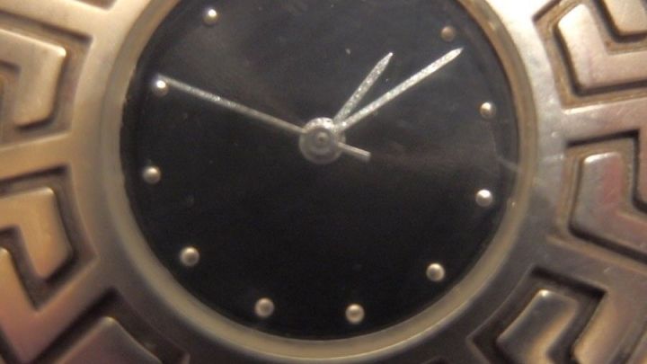 Eine stilvolle Wanduhr mit einem zierenden Geh&auml;use zeigt innen beschlagene Uhrenglasscheiben in einem ged&auml;mpften Licht.
