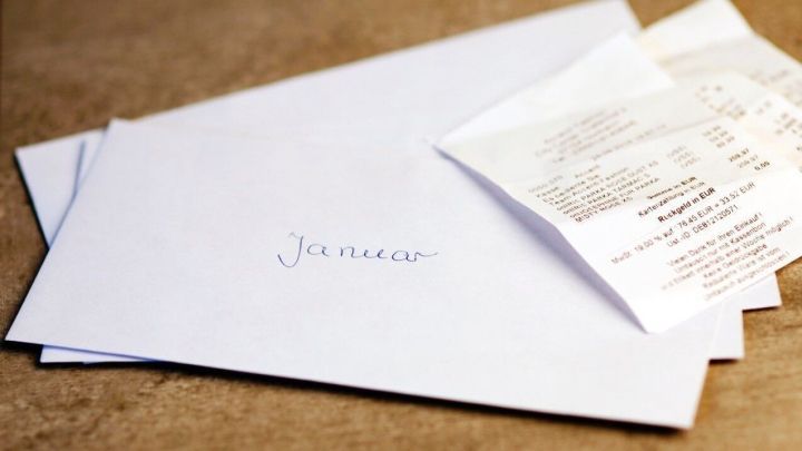 Ein Umschlag mit &bdquo;Januar&ldquo; liegt auf einem Tisch, daneben stecken Kassenzettel, die teilweise sichtbar sind.