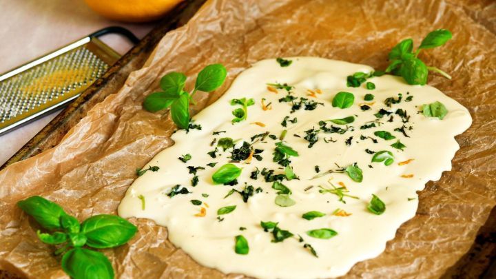 Eine wei&szlig;e Schokolade mit frischem Zitronen- und Basilikum-Geschmack liegt auf Backpapier, umgeben von frischen Kr&auml;utern.