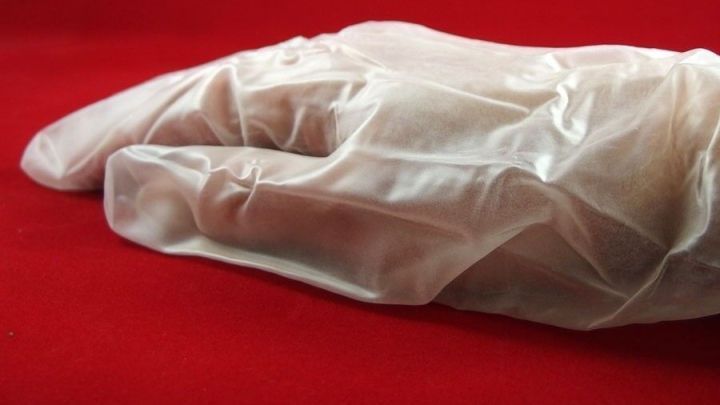 Ein transparenter Gummihandschuh liegt flach auf einem roten Hintergrund, bereit f&uuml;r hygienische Aufgaben ohne L&ouml;cher.