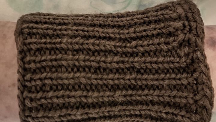 Ein gestrickter Stulpen umgibt einen Arm, w&auml;hrend er wohlig auf einer weichen Oberfl&auml;che liegt, um kalte H&auml;nde zu w&auml;rmen.