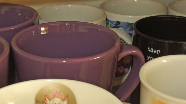 Eine lila Tasse steht eng zwischen weiteren Tassen und Geschirr im &uuml;berf&uuml;llten K&uuml;chenschrank.