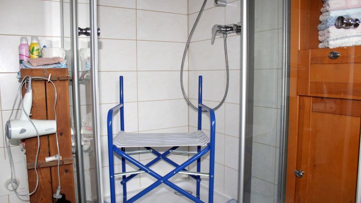 Ein blauer Hocker steht in einer Dusche, umgeben von Fliesen und Duscharmaturen, bereit zur Nutzung.