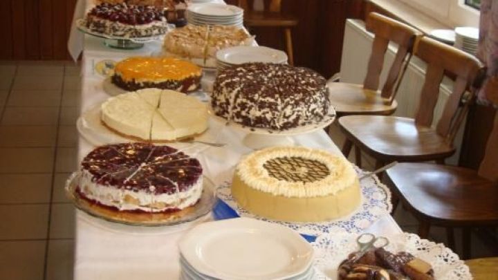 Eine dekorative Eiskaffee-Sahnetorte steht auf einem gedeckten Tisch mit vielen weiteren Kuchen und Tellern.