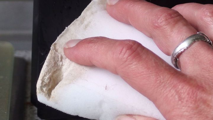 Eine Hand reinigt die Au&szlig;enseite einer Fritteuse mit einem feuchten Tuch, um Fett und Schmutz zu entfernen.