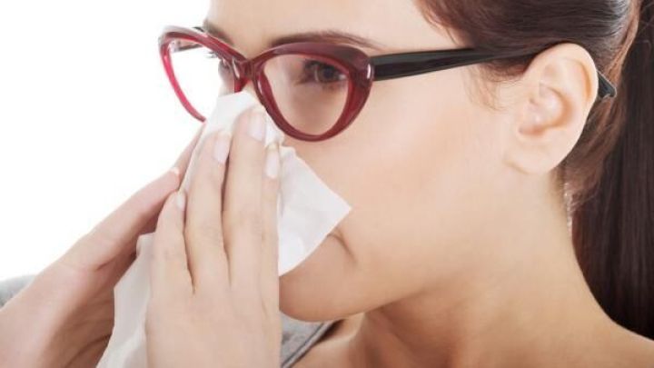 Frau mit roter Brille schn&auml;uzt sich in ein Taschentuch. Helle Umgebung.