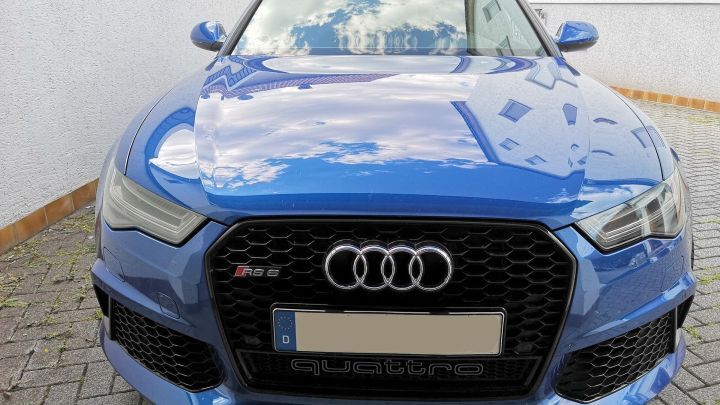 Das blaue Auto gl&auml;nzt auf dem gepflasterten Hof. Die Motorhaube spiegelt den Himmel und Geb&auml;ude wider. Text: "quattro".