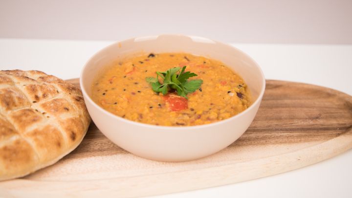Cremiges Daal mit Tomaten und Gew&uuml;rzen, im Bild mit frischer Kr&auml;uter-Garnitur und Fladenbrot serviert.