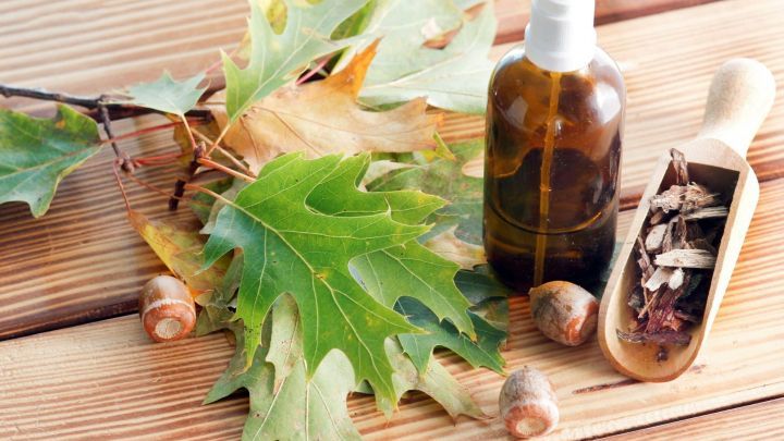 Ein Braunglasfl&auml;schchen mit Spraydeckel steht neben Eichenbl&auml;ttern und einer Holzschaufel mit Rinde auf einer Holzoberfl&auml;che.