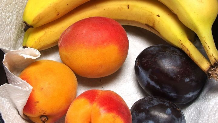 Bunte Fr&uuml;chte, darunter Bananen und Pfirsiche, liegen auf einem wei&szlig;en Tuch und sind bereit f&uuml;r den Genuss oder die Verteilung.