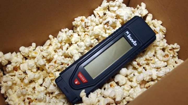 Eine schwarze digitale Messger&auml;t liegt auf einer F&uuml;llung aus Popcorn in einem Karton, der f&uuml;r Verpackungszwecke genutzt wird.