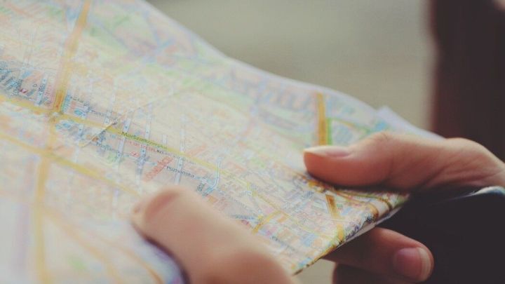 Eine Person h&auml;lt einen Stadtplan in der Hand und sucht darauf nach Wegen, w&auml;hrend sie in einer st&auml;dtischen Umgebung steht.