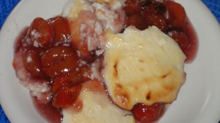 Kleckser aus Kirsch-Quark-Auflauf auf einem wei&szlig;en Teller, umgeben von einem blauen Untergrund.