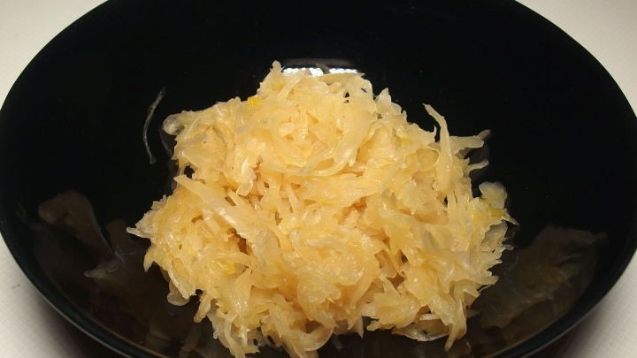 Eine schwarze Sch&uuml;ssel enth&auml;lt frisch geriebenes Sauerkraut, das bereit ist, zu Bratw&uuml;rsten bei der Grillparty serviert zu werden.