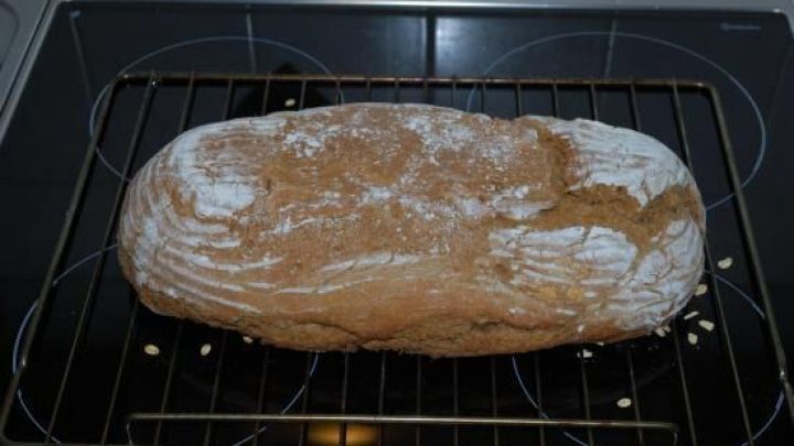 Ein frisch gebackenes 2-Korn-Vollkornbrot liegt auf einem Rost im Ofen, umgeben von leeren Herdplatten.