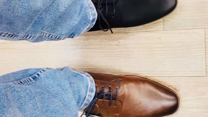 Schwarzer und brauner Schuh an den F&uuml;&szlig;en einer Person stehen auf einem Holzboden, w&auml;hrend sie sich f&uuml;r den Schuhkauf entscheiden.