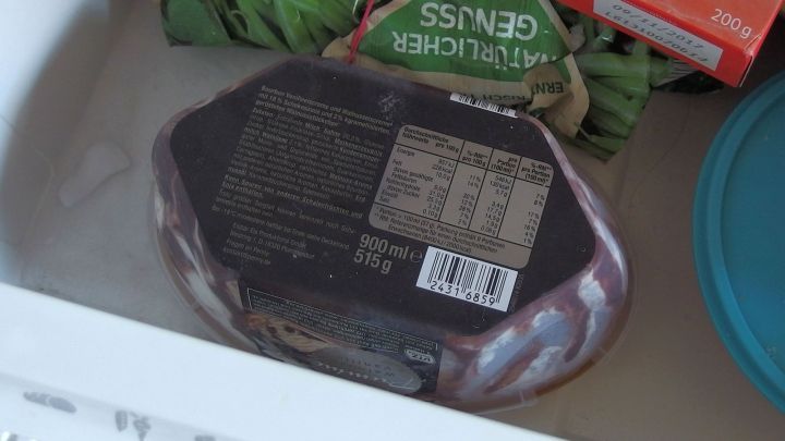 Eine Verpackung von Speiseeis mit Inhaltsangaben liegt im Gefrierfach, umgeben von anderen gefrorenen Lebensmitteln.