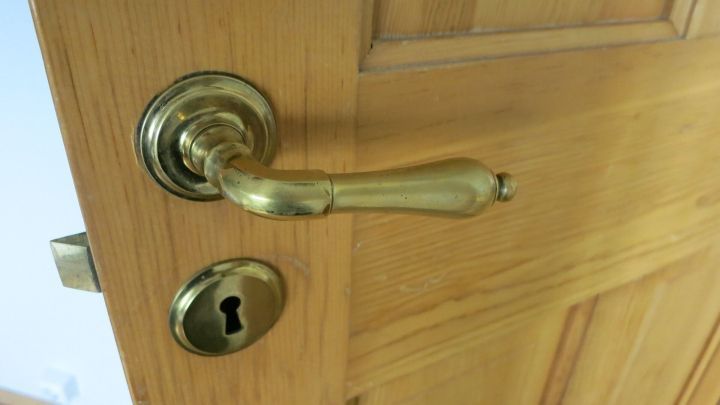 Eine T&uuml;rklinke aus gl&auml;nzendem Messing steht an einer Holzt&uuml;r, bereit, ge&ouml;ffnet zu werden. Der Kontext ist ein heller Raum.